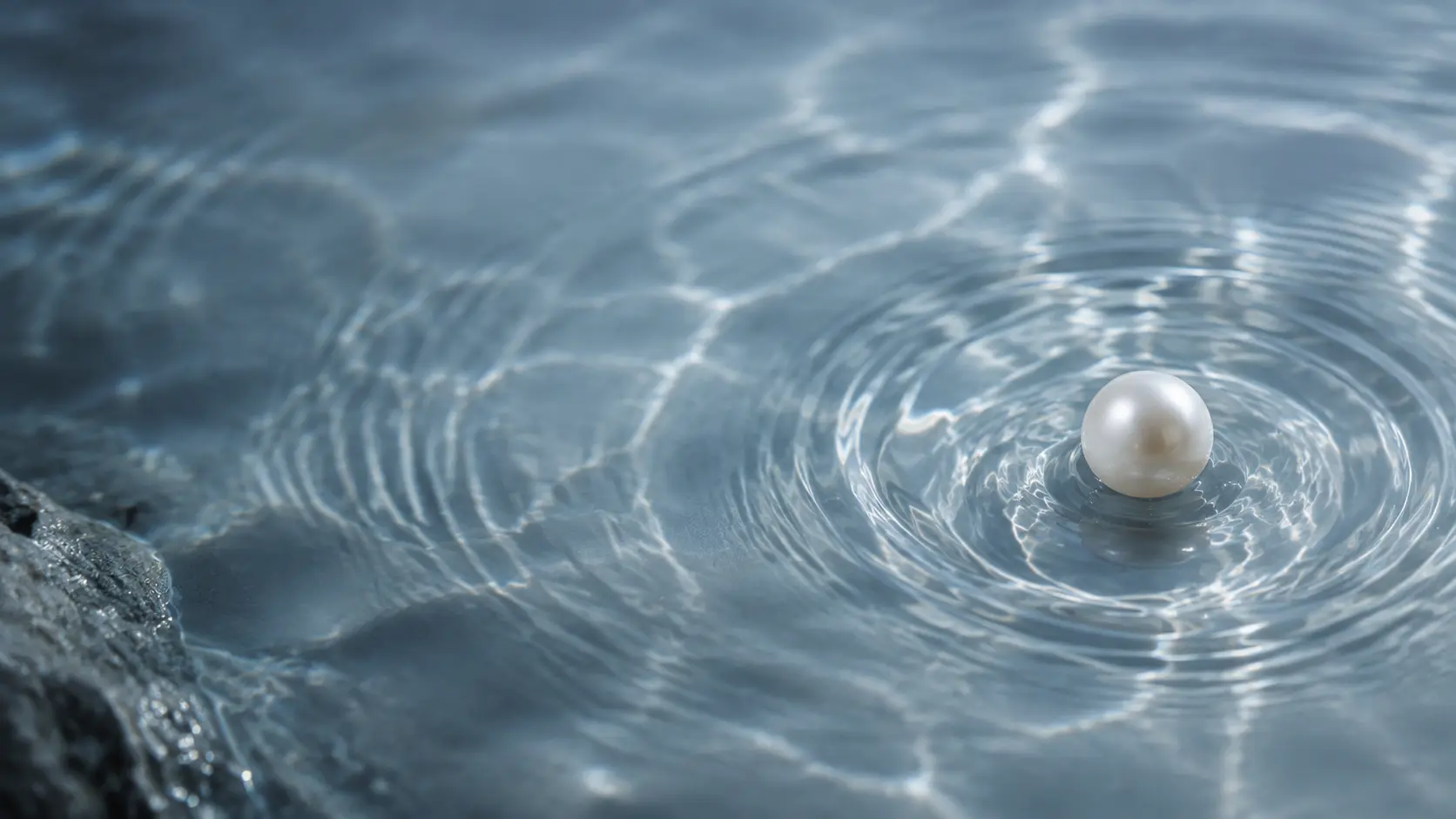 A luminous pearl surrounded by gentle ripples in mineral blue water